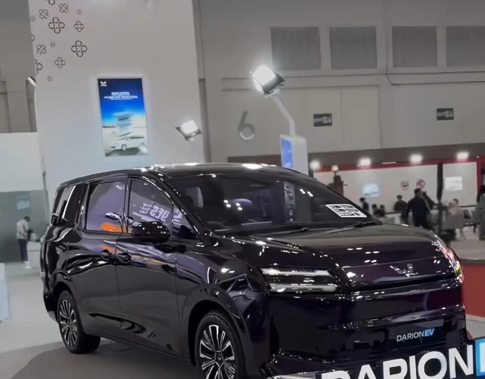 Black multi-purpose vehicle on a showroom floor with a large DARION EV sign in front and bright exhibition lights above.