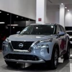 Silver Nissan SUV on display in a bright car showroom with a glossy tiled floor.
