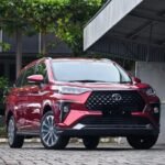 snaptik-app-7636452415373397266-slide-1 - Dyantransport Front three-quarter view of a red Toyota SUV with a bold black grille parked on a cobblestone driveway under a metal carport.