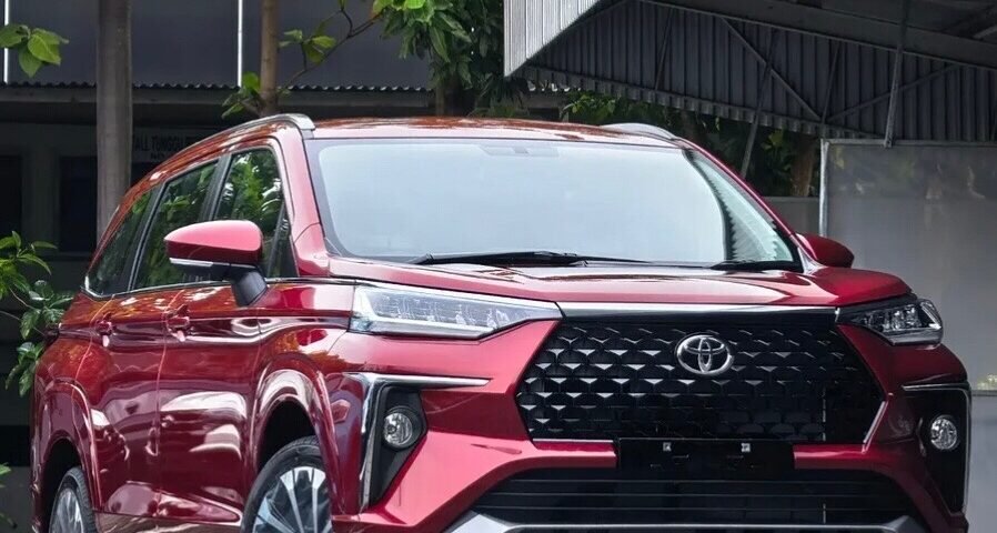 snaptik-app-7636452415373397266-slide-1 - Dyantransport Front three-quarter view of a red Toyota SUV with a bold black grille parked on a cobblestone driveway under a metal carport.