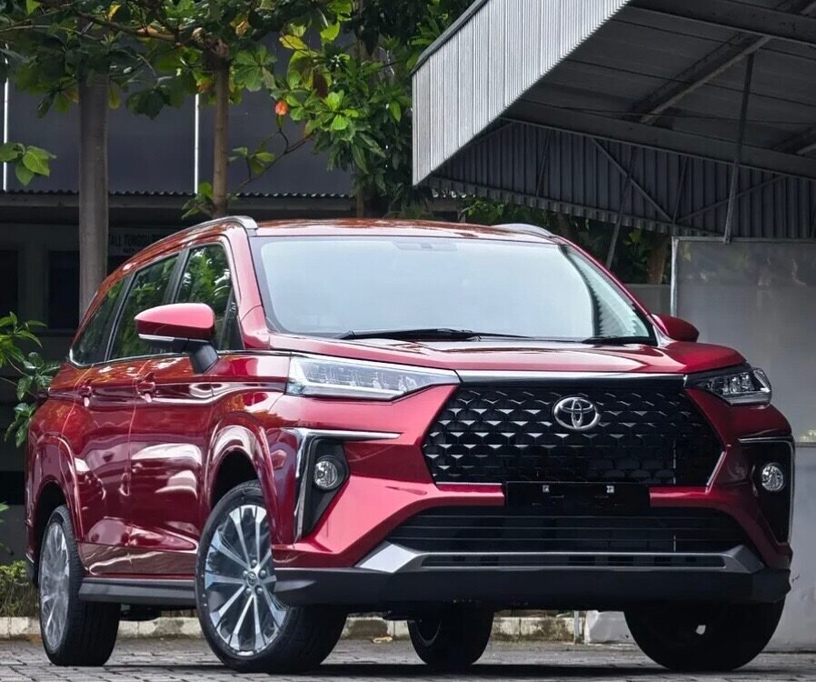 Front three-quarter view of a red Toyota SUV with a bold black grille parked on a cobblestone driveway under a metal carport.