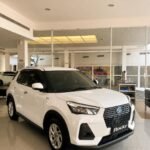 snaptik-app-7644405953135119624-slide-2 - Dyantransport White compact SUV on a showroom floor, facing forward with a bold black grille and 'Rocky' license plate.