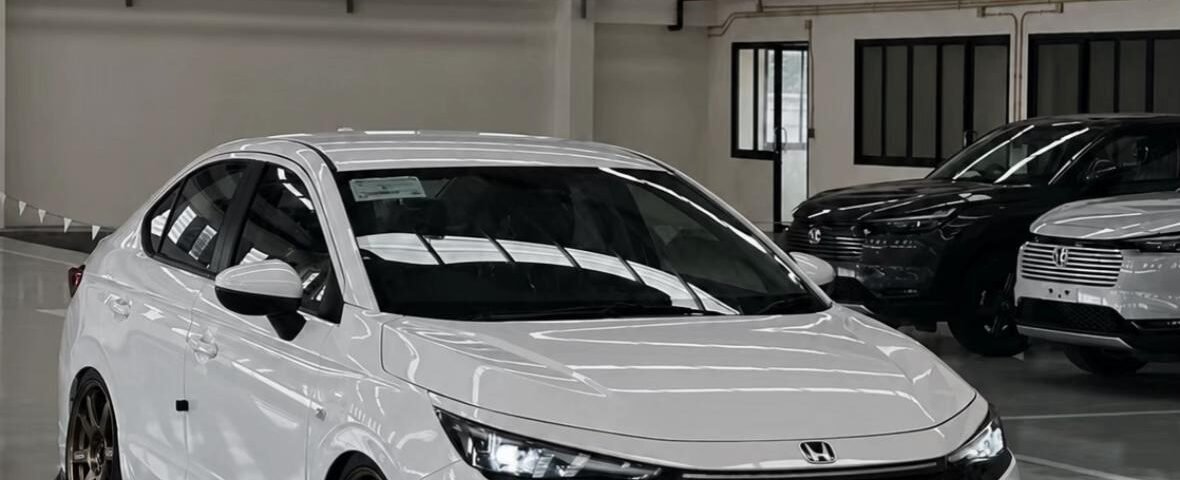 White Honda sedan with bronze aftermarket wheels and lowered suspension in a showroom setting.