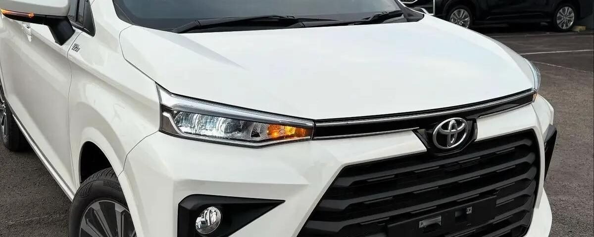 White Toyota SUV in a parking lot viewed from the front-left, with other cars and a metal building in the background.