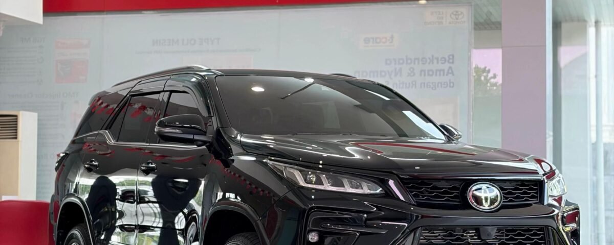 Black Toyota Fortuner on showroom floor, glossy finish, front grille visible, reflections on polished tiles behind glass walls